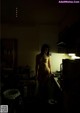 A naked woman standing in a kitchen next to a sink.